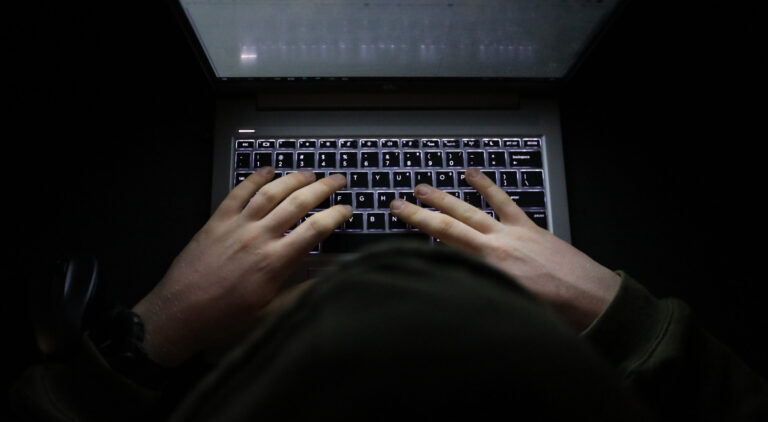 Person with a hoody typing at a computer in the dark. Suspicious online behavior