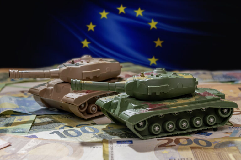 Close up of toy tanks against the background of unfolded euro notes and the European flag