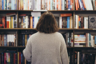 Young brunette woman choosing a book in a bookstore, back view.