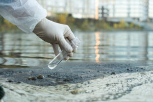 Female ecologist in protective glove holding a test tube with water from a city river