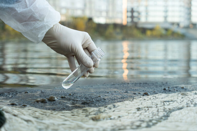 Female ecologist in protective glove holding a test tube with water from a city river