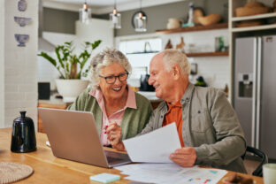 Happy old couple managing home finances on laptop