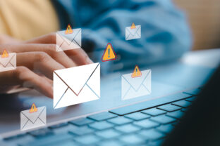 Hands typing on a laptop with warning email icons, representing phishing attacks, scam messages, and email security threats in a digital communication concept.