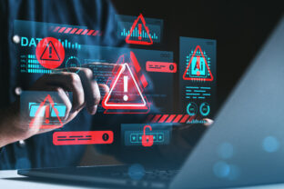 Cybersecurity threat warning concept with holographic red alert symbols over hands using laptop in dark environment, illustrating data protection risks.