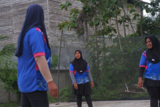 Girls wearing sports uniforms and hijabs playing volleyball on an outdoor court