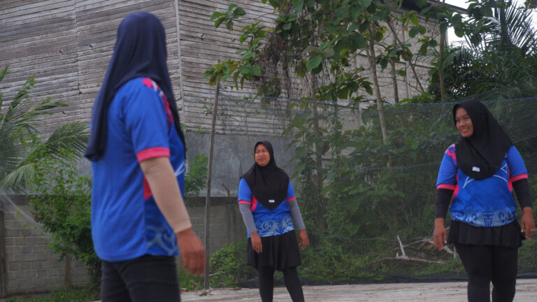 Girls wearing sports uniforms and hijabs playing volleyball on an outdoor court