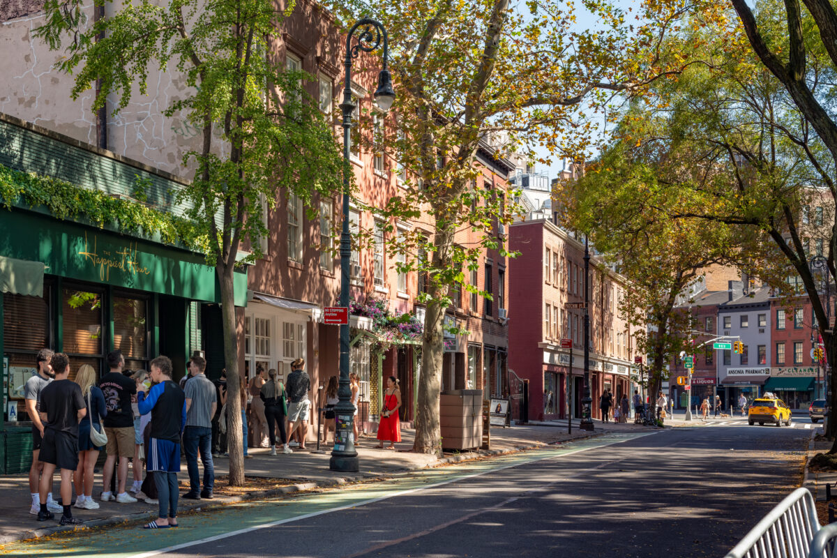 A sunny Sunday in West Village, Manhattan, with people gathering outside a cafe and historic brick buildings lining the street.