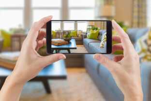 Female Hands Holding Smart Phone Displaying Photo of House Interior Living Room Behind.