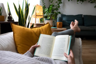 POV of young woman relaxing at home reading a book lying on sofa