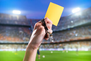 Hand of referee with yellow card and whistle