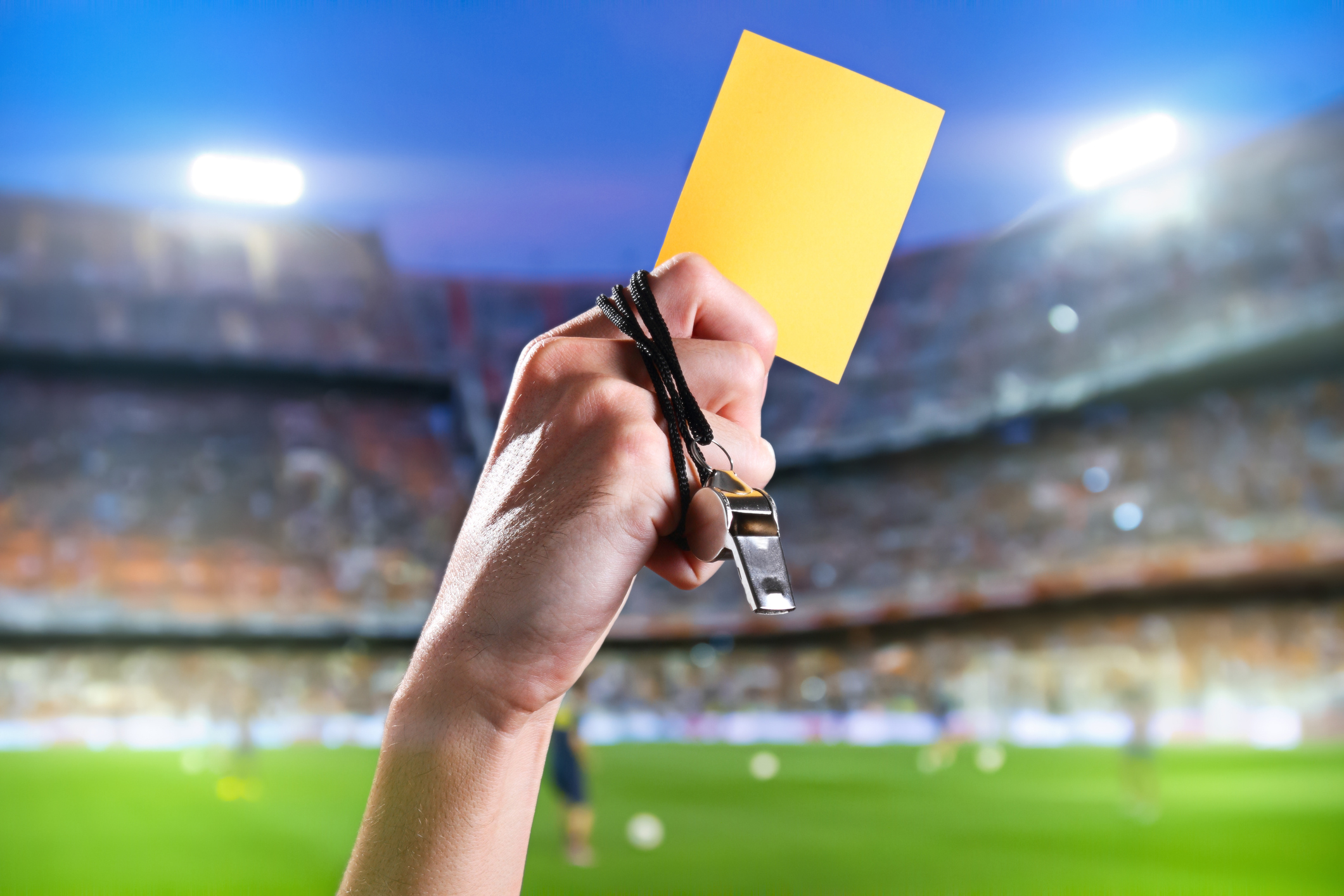 Hand of referee with yellow card and whistle