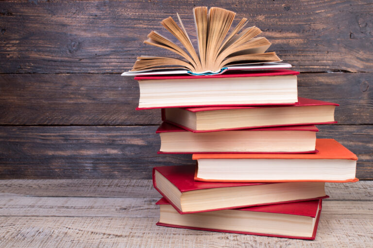 Composition with hardback books, fanned pages on wooden deck table and background. Books stacking. Back to school. Copy Space. Education background.