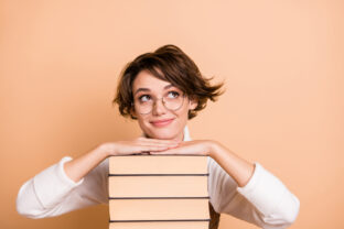 Photo portrait of schoolgirl dreaming near books pile looking blank space isolated on pastel beige color background