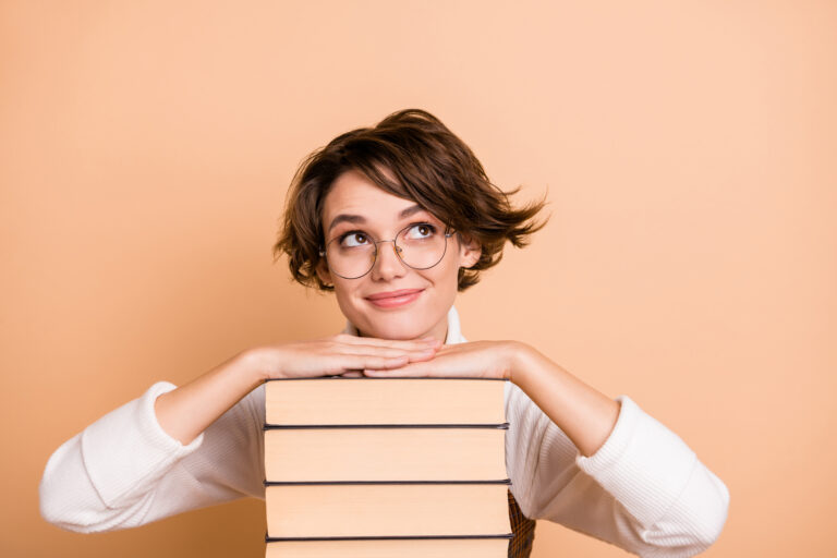 Photo portrait of schoolgirl dreaming near books pile looking blank space isolated on pastel beige color background