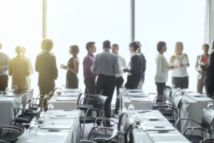 Group of people standing by windows of conference room, socializing during coffee break