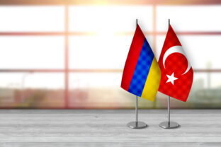Armenian and turkish 3D desk flags are standing together on a desk in front of sunny background with large copy space.
