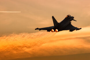A Spanish Air Force Eurofighter Typhoon doing aerial maneuvers at sunset with orange background.