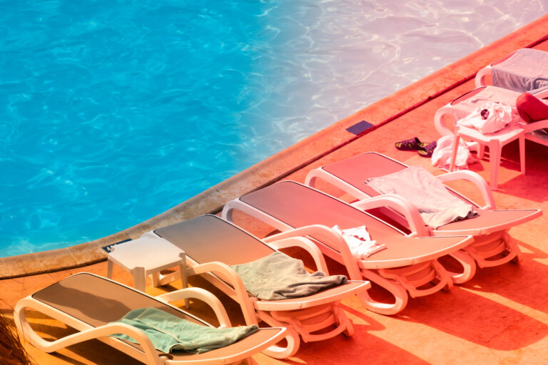 Sun loungers by the pool at sunset. Perfect beach sunset, relaxation pool in a luxurious beachfront hotel resort in sunset light. Sunset beach landscape. Loungers palm tree infinity pool reflections