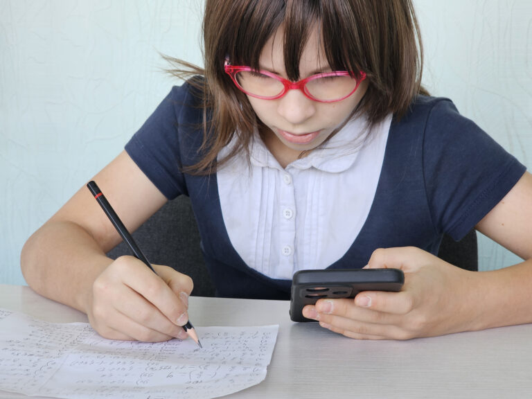 Serious kid doing classwork using smartphone in class and mobile education