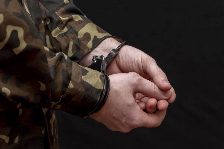 A military man in camouflage is handcuffed on a dark background. Concept: war criminal, prisoner of war, tribunal for deserters, traitor to the motherland.