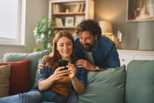 Happy couple relaxing on sofa and browsing smartphone at home