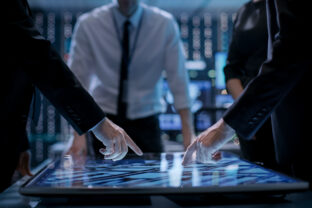 Corporate Managers Working at the Table in Monitoring Room. Room is Full of State of the Art Technology. Computers with Animated Screens.