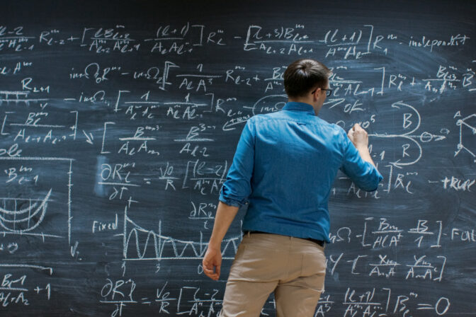 Brilliant Young Mathematician Is Writing on Big Blackboard and Thinking about Solving Long and Complex Equation/ Formula.