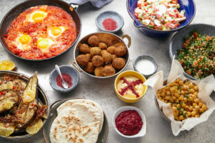 Overhead image of traditional jewish and middle eastern food: falafel, fattoush, tabouli, shakshuka, balila, hummus, roasted eggplants and spicy beetroot dip. Israeli cuisine concept