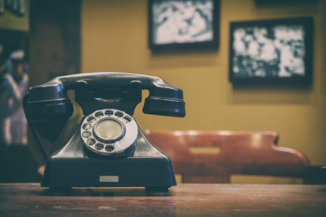 Old style telephone on working desk with blurred background of photo hanging on wall, vintage tone