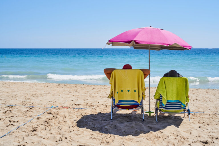 Parasol, two chairs and towels on sand beach while tourists having bath in sea in summer