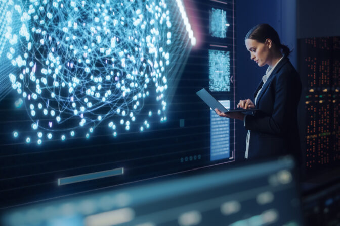 Young Female Computer Science Engineer Working on Laptop next at Big Screen Display Showing Neural Data. Telecommunications Technology Company System Control and Monitoring Room with Servers.