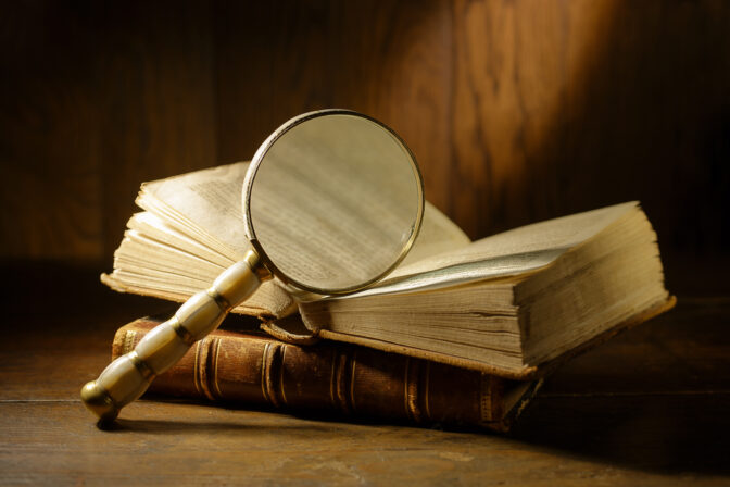 Open antique book with magnifying glass. Concept for learn history, investigation, find artifacts.