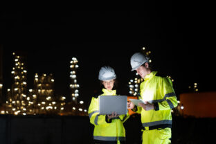 Team of Engineers Working at Oil Storage Facility at Night, Industrial Workers Discussing Operations with Laptop at Site, Professional Engineers Collaborating at Petroleum Storage Tanks