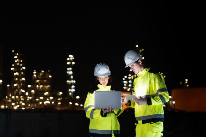 Team of Engineers Working at Oil Storage Facility at Night, Industrial Workers Discussing Operations with Laptop at Site, Professional Engineers Collaborating at Petroleum Storage Tanks