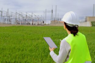 Female engineer inspecting an electrical power station, using a digital tablet for data collection and analysis while ensuring efficient and sustainable energy infrastructure operations