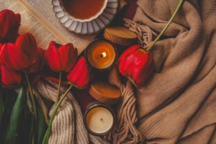 Cozy scene with red tulips, lit candles, a cup of tea, and a book