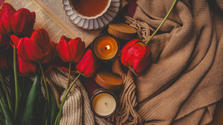 Cozy scene with red tulips, lit candles, a cup of tea, and a book