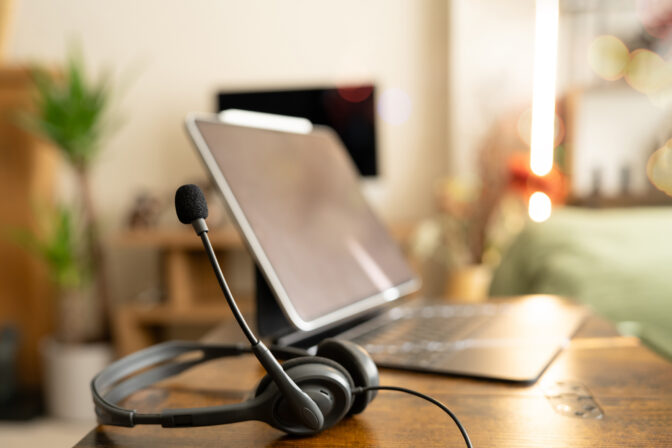 Headset and laptop on wooden desk in cozy home office. Remote support, online communication, virtual meeting, customer service, and hybrid work concept with warm evening lighting
