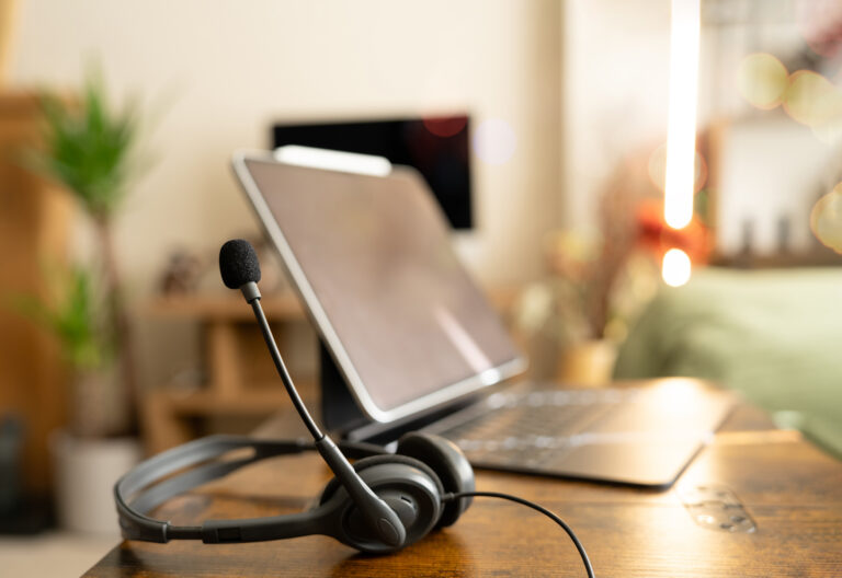 Headset and laptop on wooden desk in cozy home office. Remote support, online communication, virtual meeting, customer service, and hybrid work concept with warm evening lighting