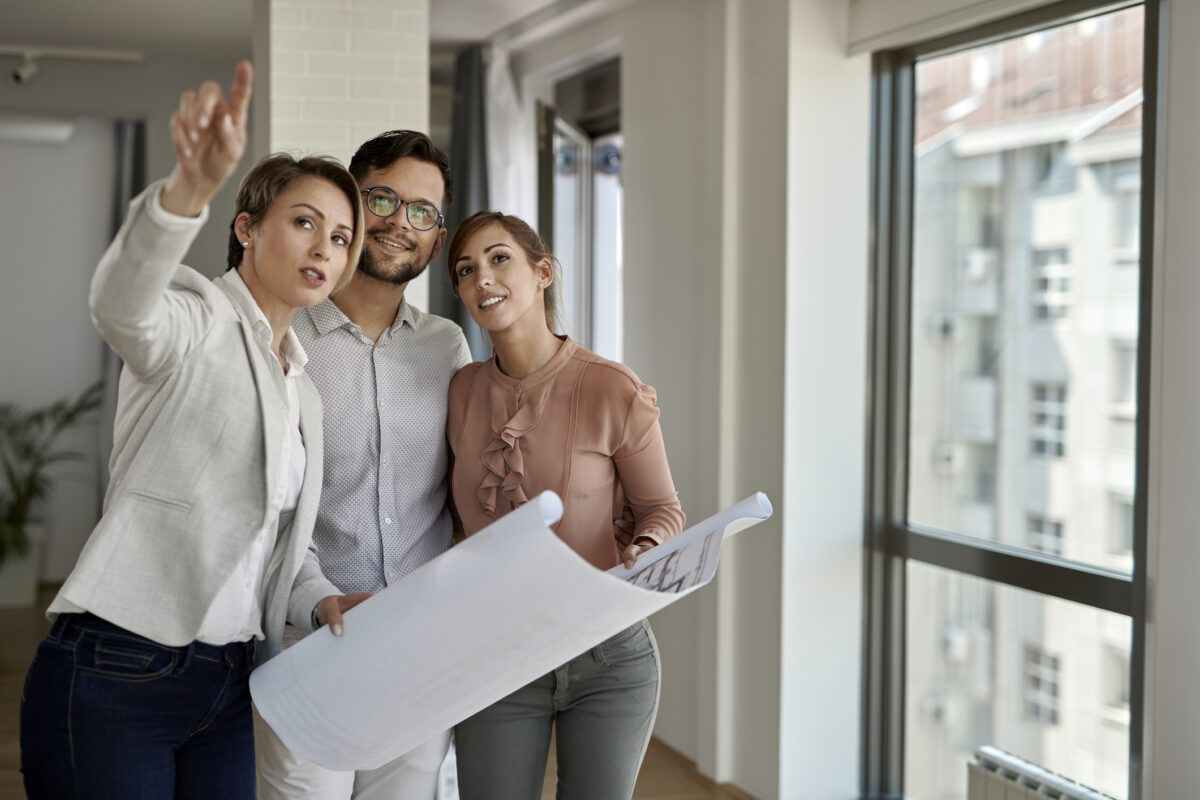 Young couple analyzing blueprints with real estate agent while buying new home.