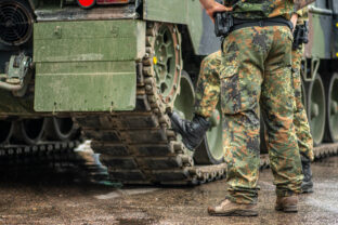 Two soldiers in camouflage uniform standing during a break under the rain near the tracks of an armoured tank