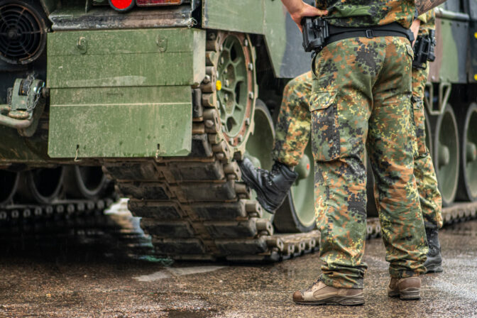 Two soldiers in camouflage uniform standing during a break under the rain near the tracks of an armoured tank