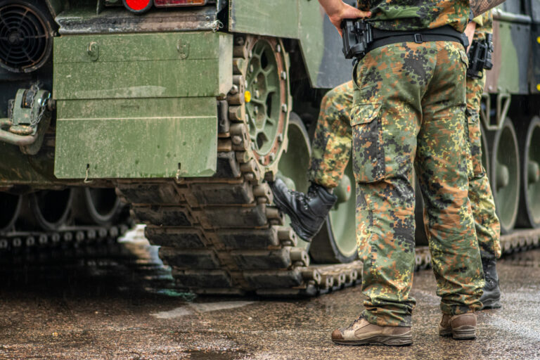 Two soldiers in camouflage uniform standing during a break under the rain near the tracks of an armoured tank