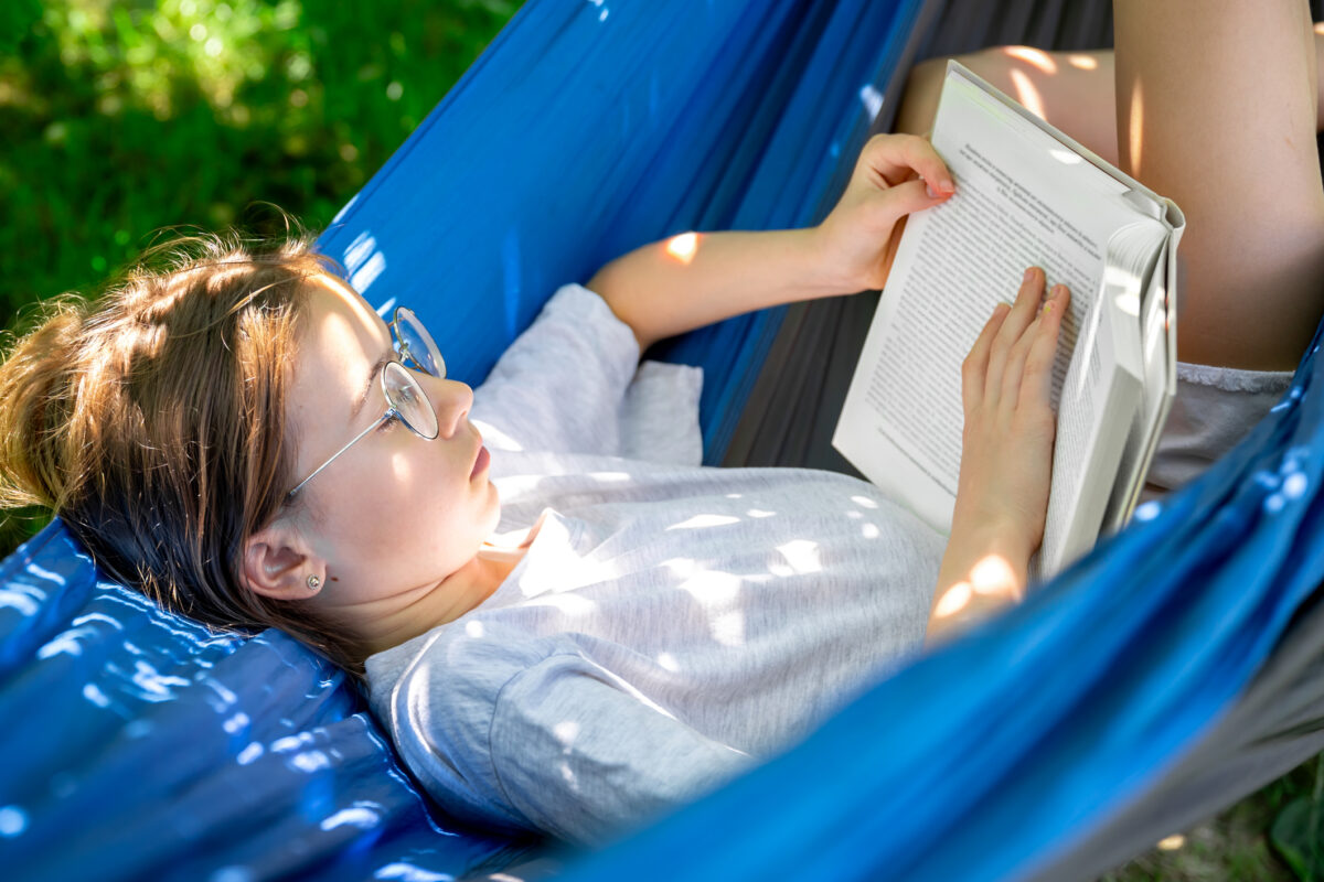 Cute girl reading a book in a hammock in the garden.