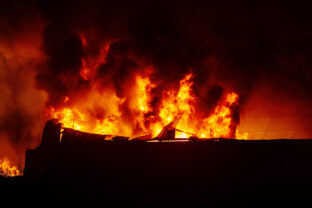 Burning industrial building. Big blaze at night, consequences of attack.