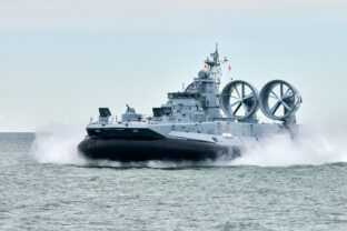 Hovercraft warship armed with armament sails into sea toward military target to attack and destroy