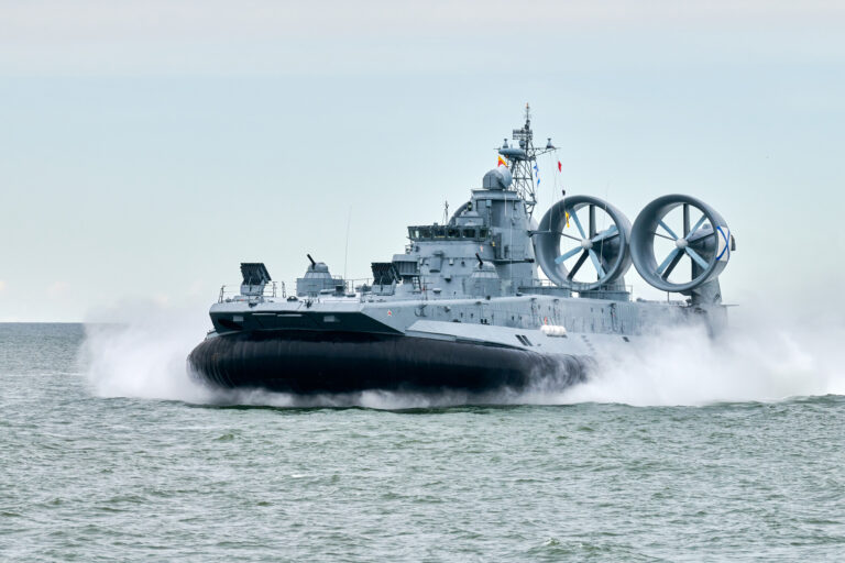 Hovercraft warship armed with armament sails into sea toward military target to attack and destroy