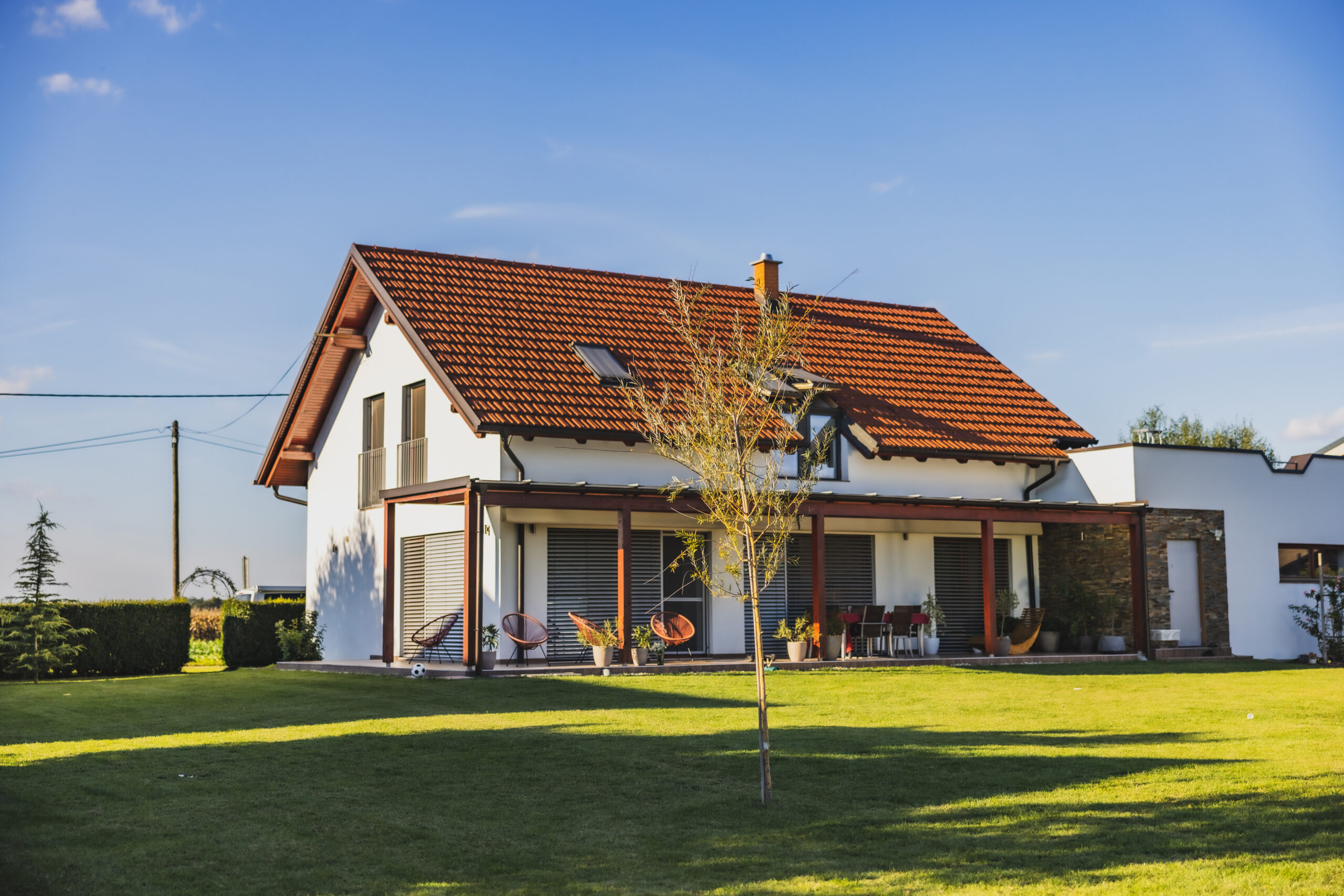 Modern house with terrace on the countryside,large backyard,young tree in front,clear sky in the background