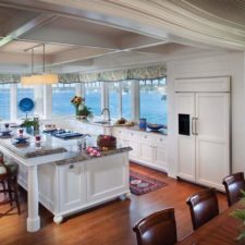 Post_large kitchen interior with white cabinetry and a big kitchen island also marble dining space with lovely stools decorated by wide windows for panoramic sea and classic lamps.jpg