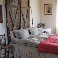 Post_bed with pillows also rustic wooden headboard with small side lamps along with round table and wooden chair decorated by wallpaper design.jpg